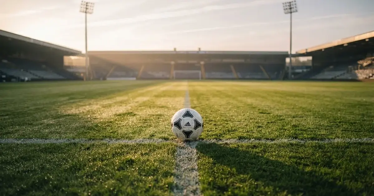 Een voetbal op de middenstip van een grasveld in het ochtendlicht