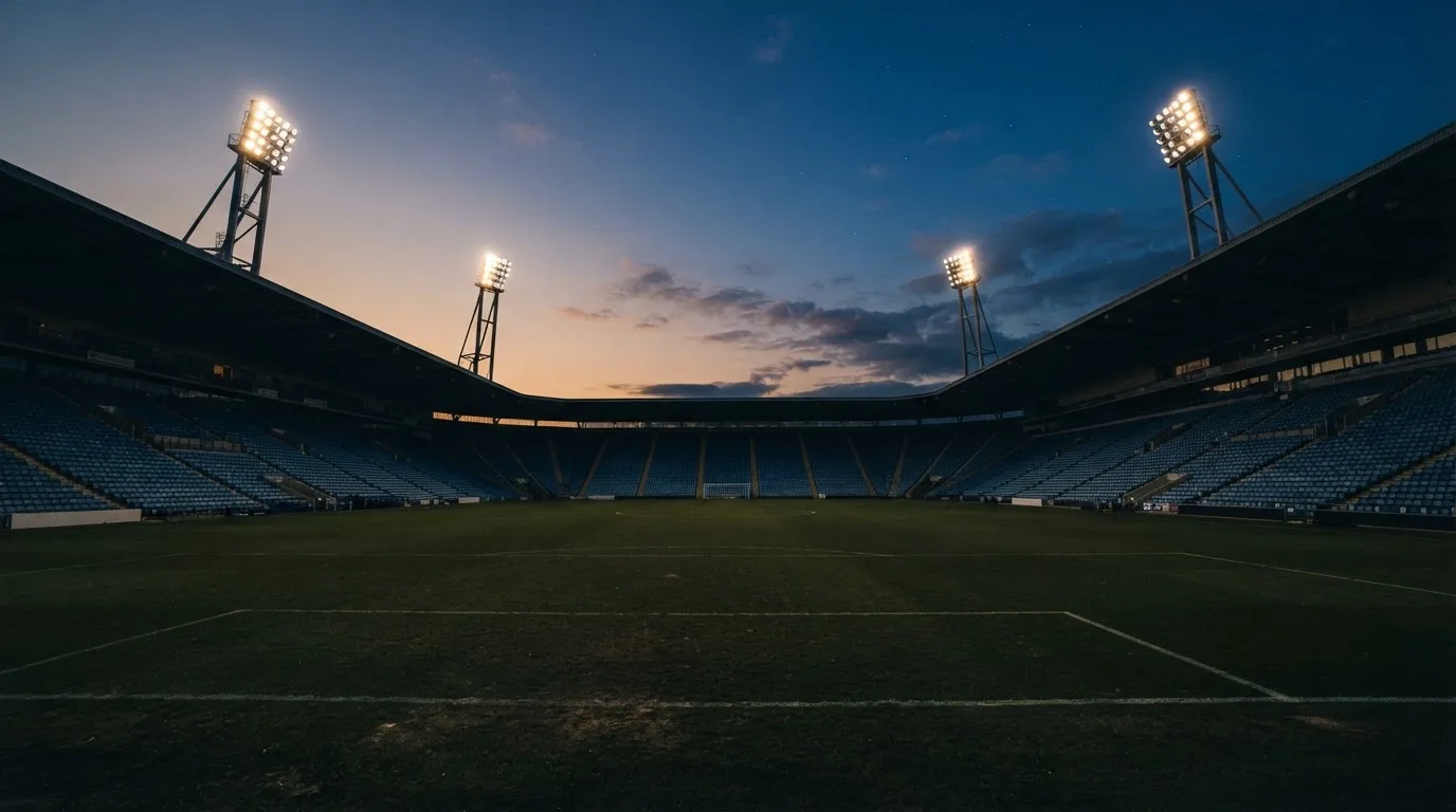 Een leeg voetbalstadion met lichtmasten bij schemering