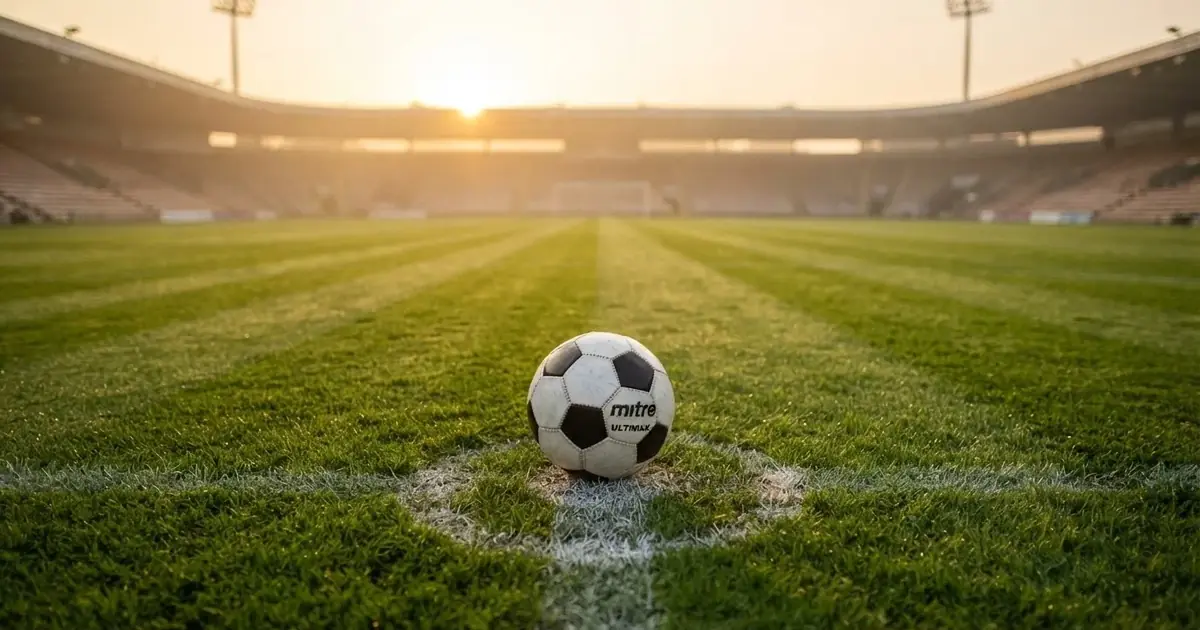 Een voetbal op de middenstip van een grasveld in het ochtendlicht